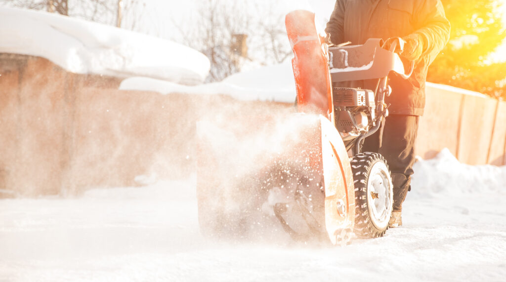 Man cleaning snow from sidewalks with snowblower machine winter.